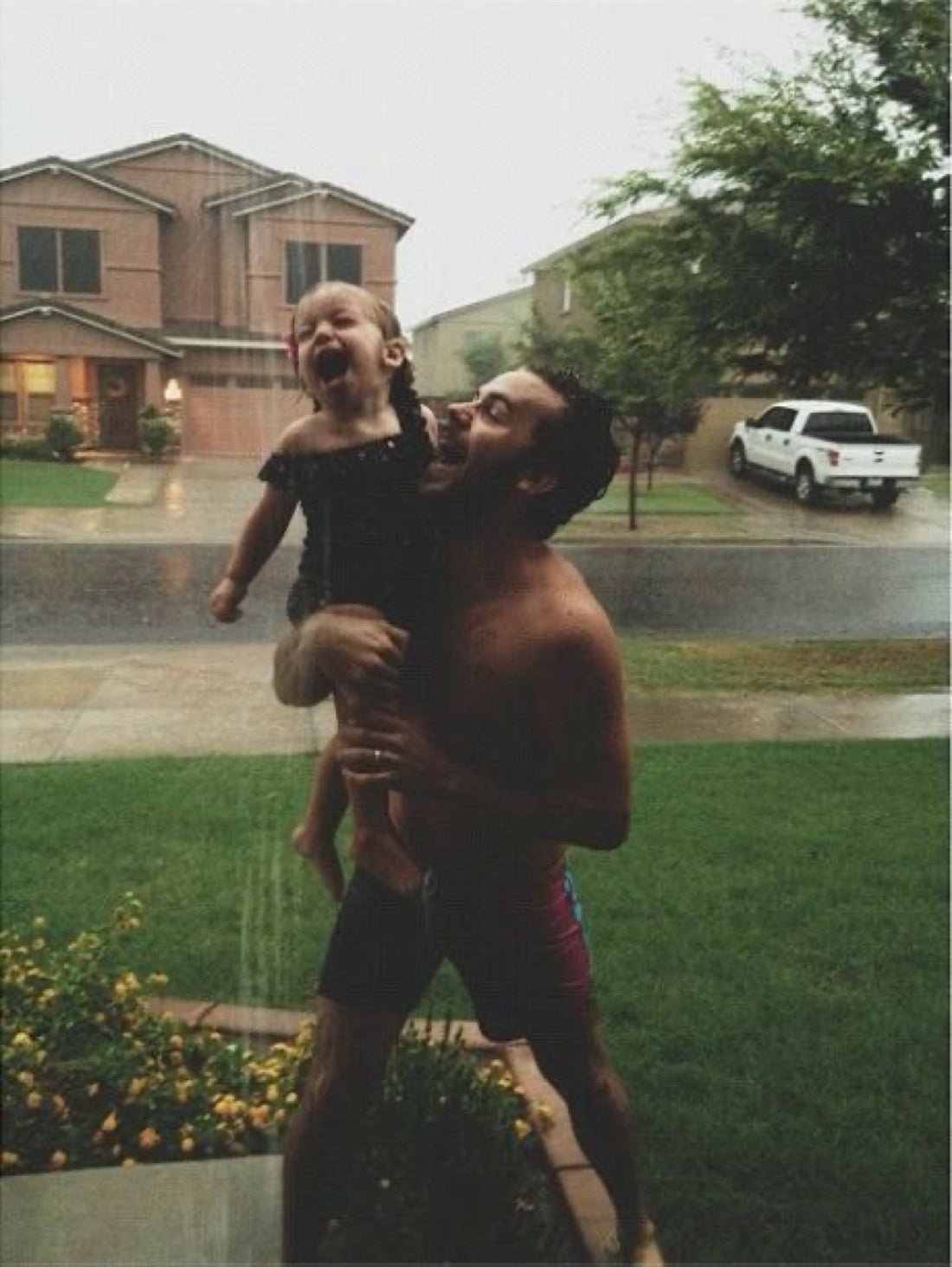 Padre sosteniendo a su hija en brazos bajo la lluvia, mirandose cara a cara y riendo