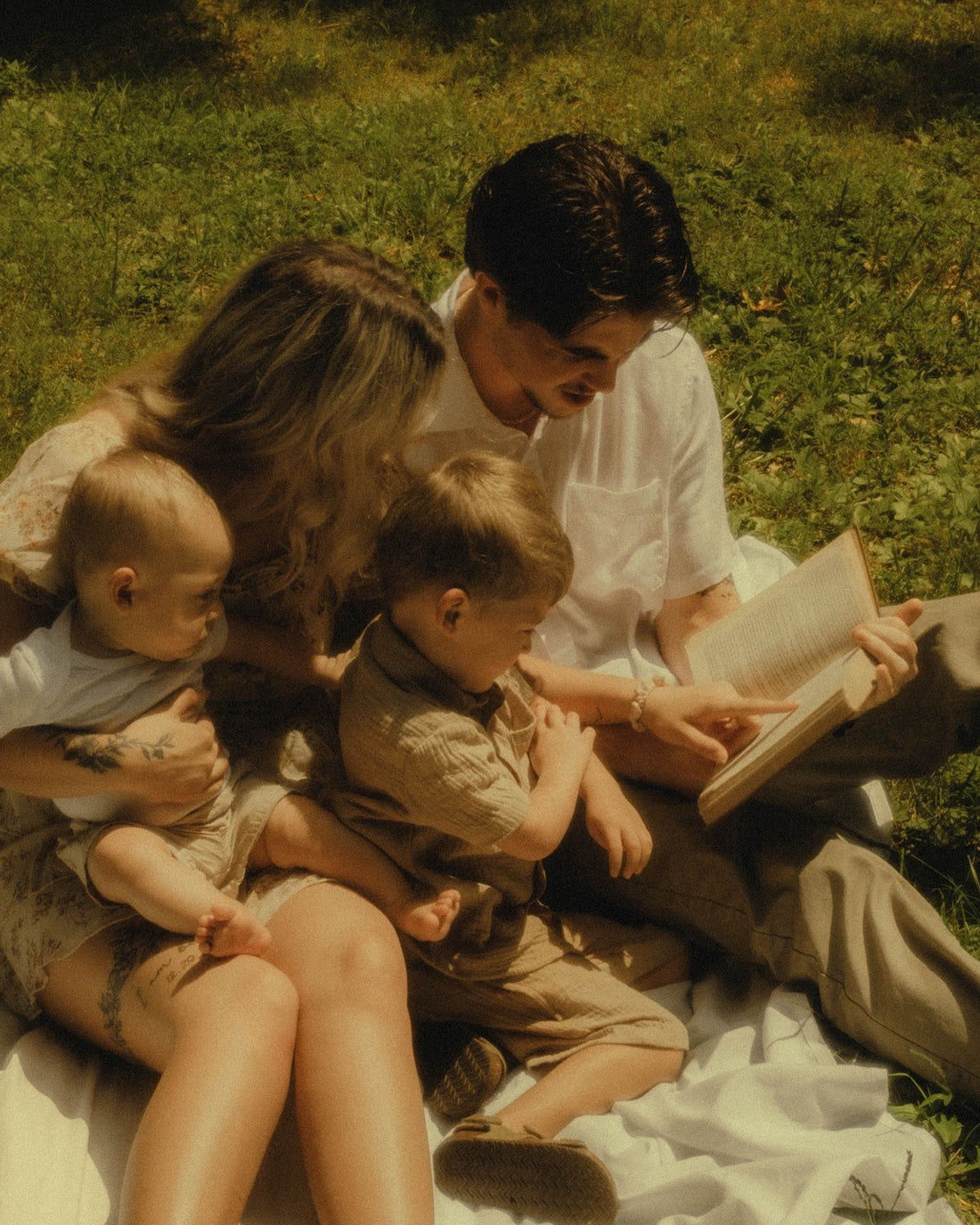 Familia leyendo un libro sobre una manta en la hierba, luz calida y ninguna pantalla